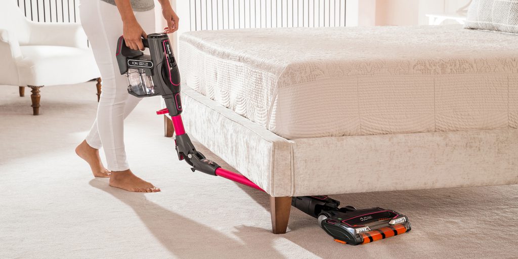 women using a vacuum cleaner to clean under bed